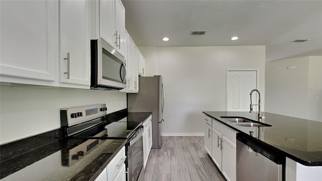 kitchen with dark stone countertops, stainless steel appliances, white cabinets, light wood-type flooring, and sink