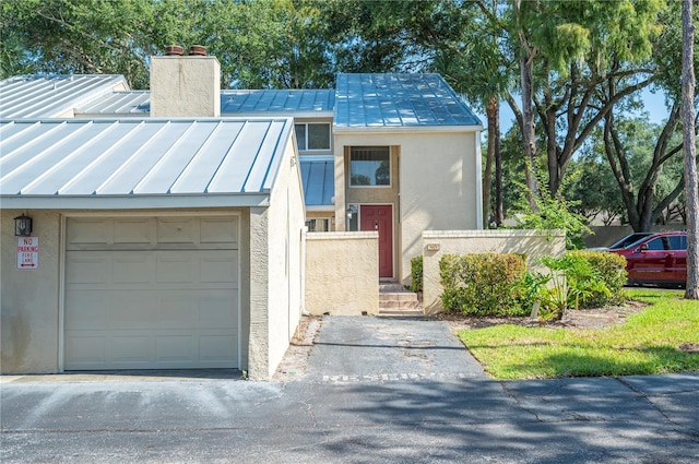 view of front of house featuring metal roof, a garage, stucco siding, a standing seam roof, and a chimney