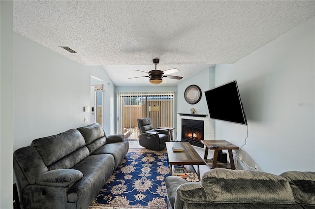 living room featuring a textured ceiling, a fireplace, visible vents, and a ceiling fan