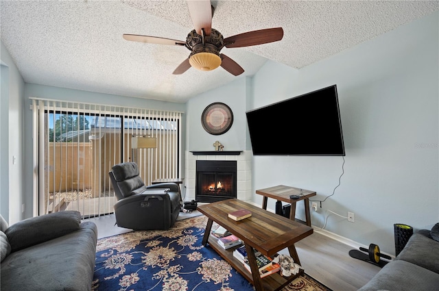 living room featuring a textured ceiling, ceiling fan, a fireplace, wood finished floors, and baseboards