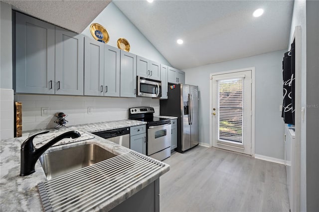 kitchen featuring lofted ceiling, decorative backsplash, appliances with stainless steel finishes, a sink, and light wood-type flooring