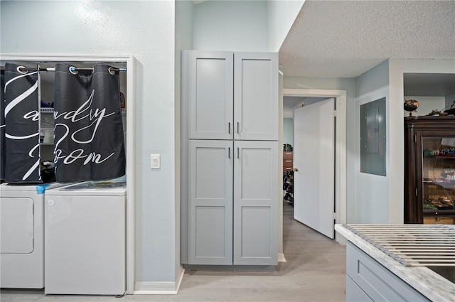 laundry room featuring light wood finished floors, electric panel, washer and clothes dryer, and a textured ceiling