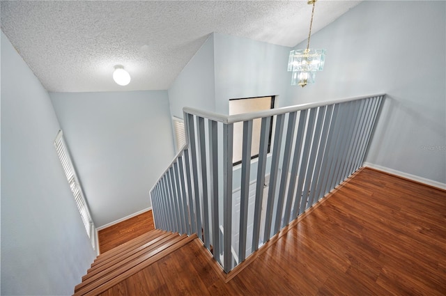 staircase with a textured ceiling, baseboards, vaulted ceiling, and wood finished floors