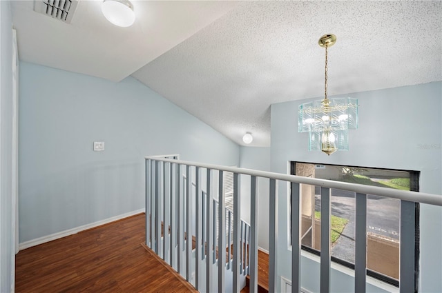 hall with visible vents, vaulted ceiling, an upstairs landing, wood finished floors, and baseboards