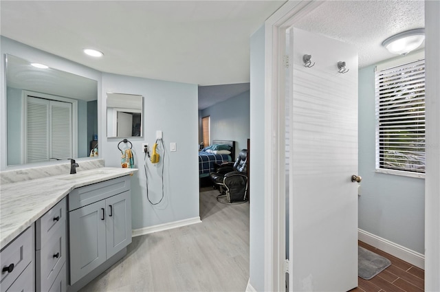 bathroom with a textured ceiling, vanity, baseboards, and wood finished floors