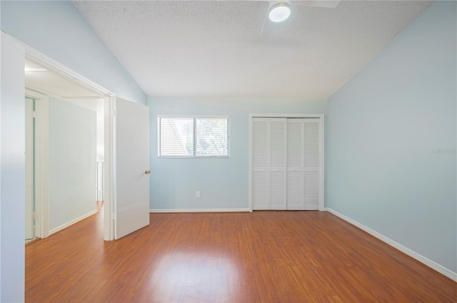 unfurnished bedroom with baseboards, lofted ceiling, wood finished floors, a textured ceiling, and a closet