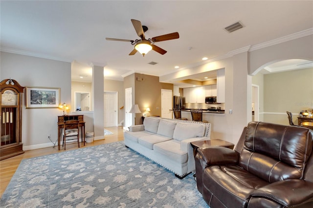 living room with arched walkways, visible vents, ornamental molding, light wood-type flooring, and baseboards