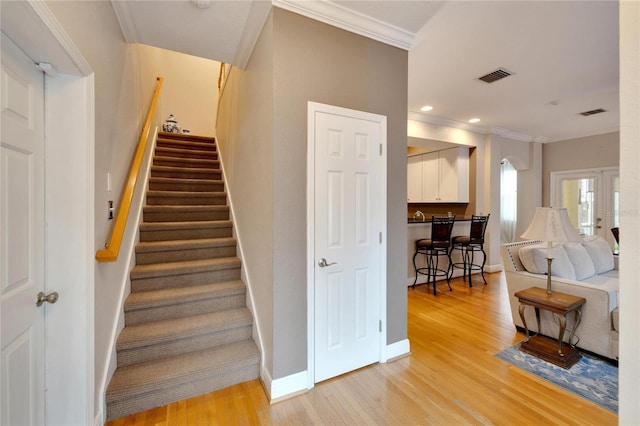 staircase with ornamental molding, wood finished floors, visible vents, and baseboards