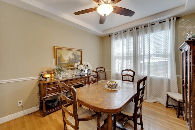 dining space featuring light wood-type flooring, a raised ceiling, ceiling fan, and baseboards