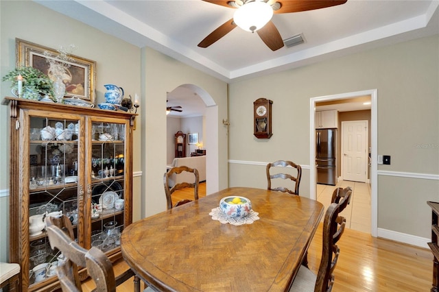 dining room featuring arched walkways, a raised ceiling, visible vents, light wood-style flooring, and ceiling fan