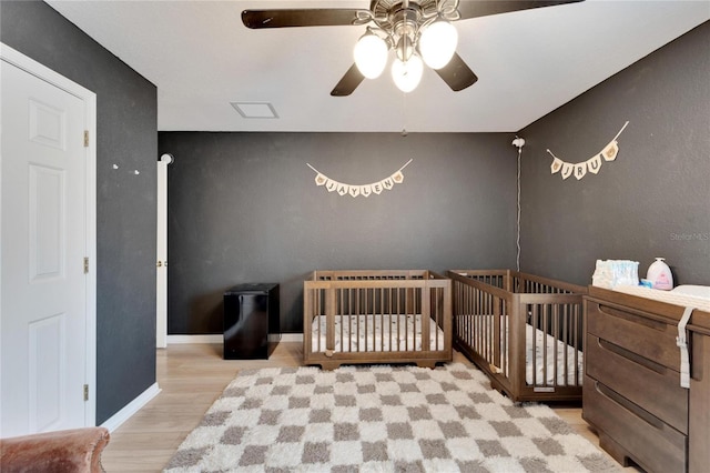 bedroom with a nursery area, ceiling fan, baseboards, and wood finished floors