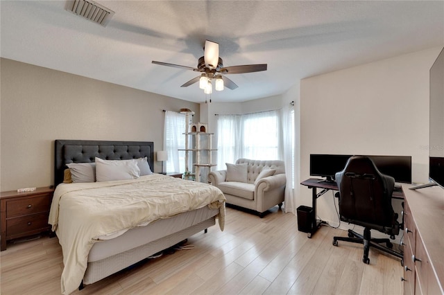 bedroom with light wood-style floors, visible vents, and a ceiling fan