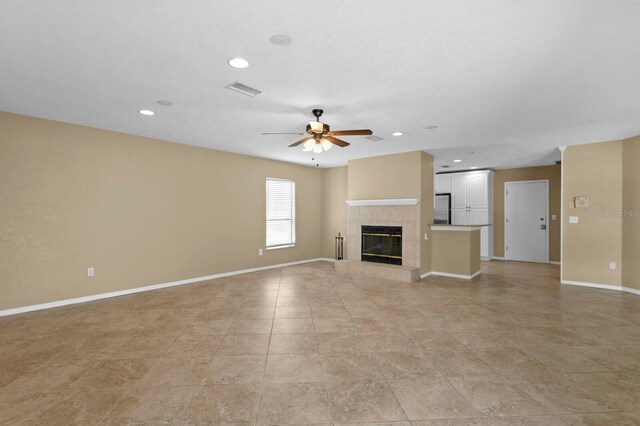 unfurnished living room with ceiling fan, light tile patterned flooring, and a tile fireplace