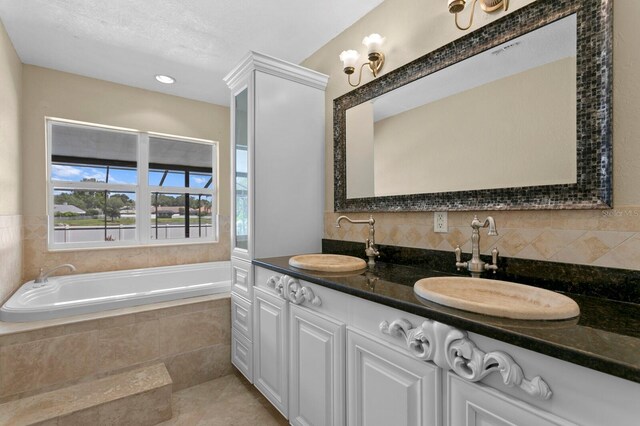 bathroom with backsplash, tiled tub, vanity, tile patterned flooring, and a textured ceiling