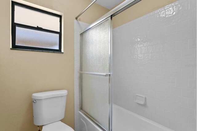 bathroom featuring combined bath / shower with glass door and toilet