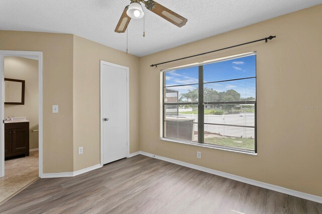 unfurnished bedroom with a textured ceiling, ceiling fan, ensuite bath, and wood-type flooring