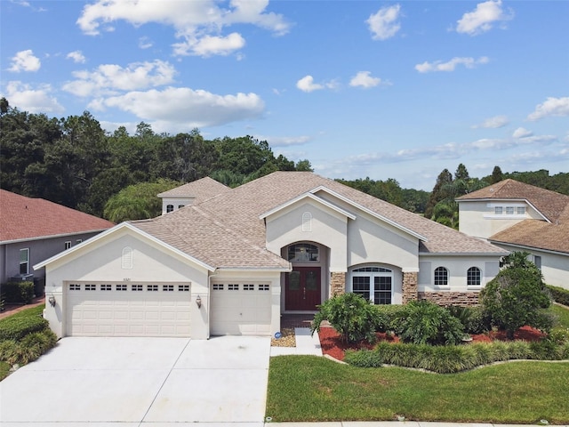 mediterranean / spanish-style house featuring a garage, concrete driveway, stone siding, stucco siding, and a front lawn