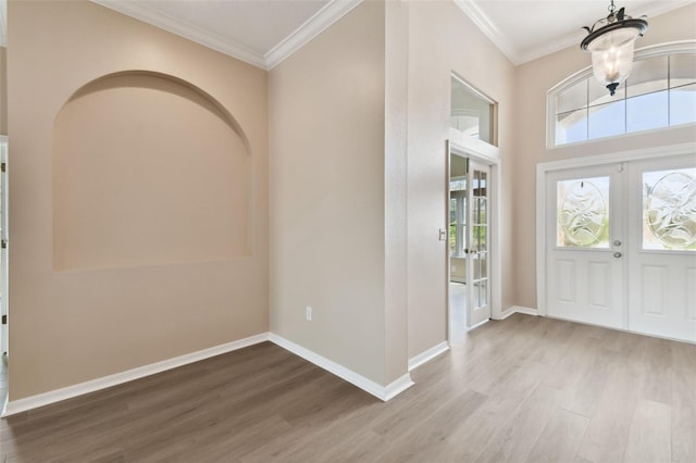 foyer featuring baseboards, wood finished floors, crown molding, and french doors