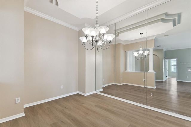 unfurnished dining area featuring an inviting chandelier, baseboards, crown molding, and wood finished floors