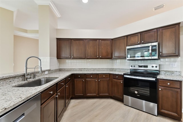 kitchen featuring light wood finished floors, stainless steel appliances, backsplash, a sink, and light stone countertops