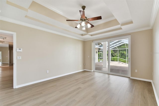 spare room with a tray ceiling, light wood-style floors, ornamental molding, ceiling fan, and baseboards