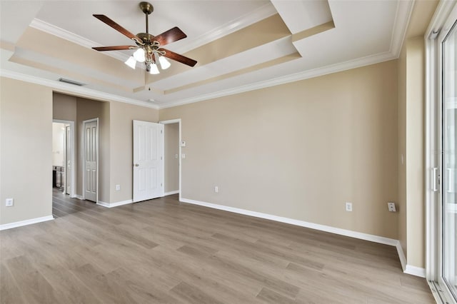 empty room with crown molding, light wood finished floors, a raised ceiling, and baseboards