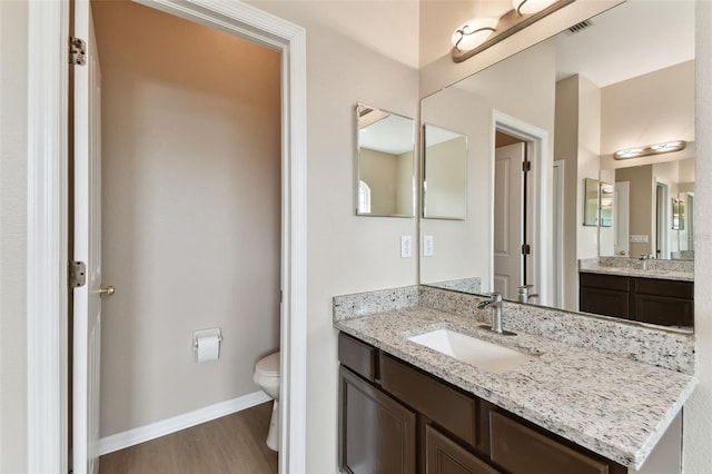 bathroom with baseboards, vanity, toilet, and wood finished floors