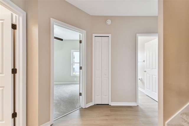 hallway with stairs, light wood finished floors, and baseboards