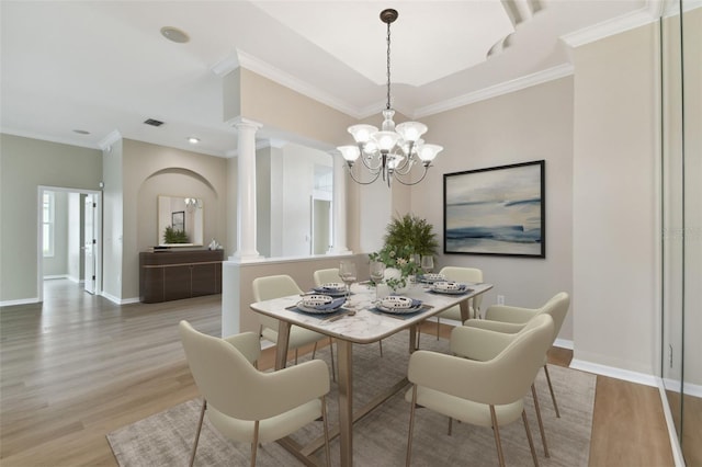 dining space featuring crown molding, baseboards, decorative columns, and light wood-style floors