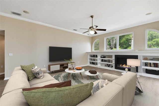 living room featuring a lit fireplace, wood finished floors, and crown molding