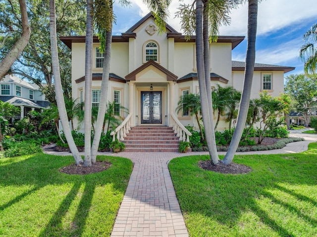 view of front of house with stucco siding, french doors, and a front yard