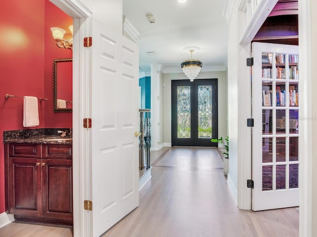 foyer featuring light hardwood / wood-style floors, sink, ornamental molding, french doors, and an inviting chandelier