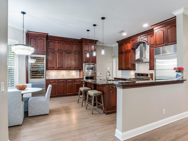 kitchen featuring decorative backsplash, appliances with stainless steel finishes, wall chimney range hood, light hardwood / wood-style floors, and a breakfast bar