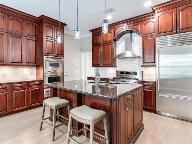 kitchen with appliances with stainless steel finishes, wall chimney range hood, tasteful backsplash, and dark stone countertops