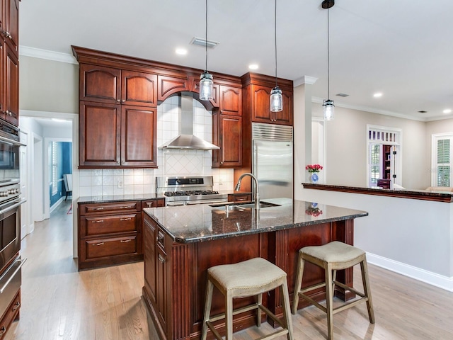 kitchen featuring appliances with stainless steel finishes, wall chimney range hood, light hardwood / wood-style floors, tasteful backsplash, and sink