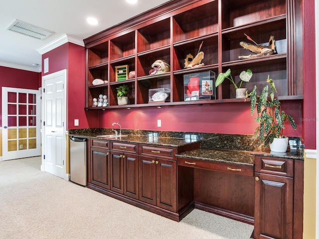 bar with dark stone counters, crown molding, dishwasher, sink, and light colored carpet