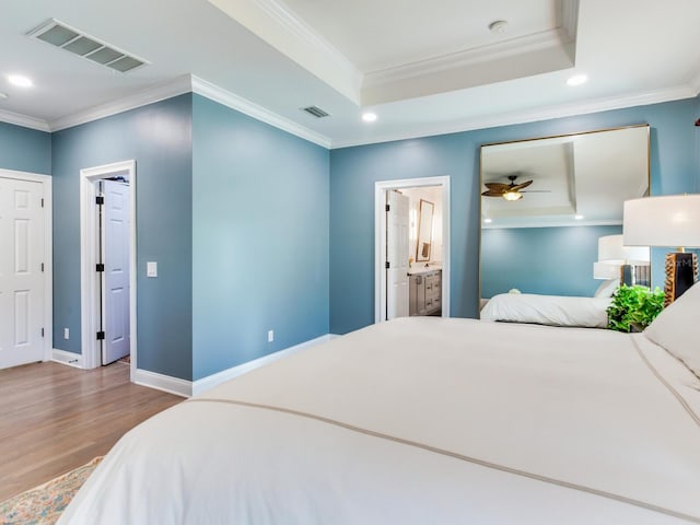 bedroom featuring crown molding, ensuite bathroom, a tray ceiling, ceiling fan, and wood-type flooring