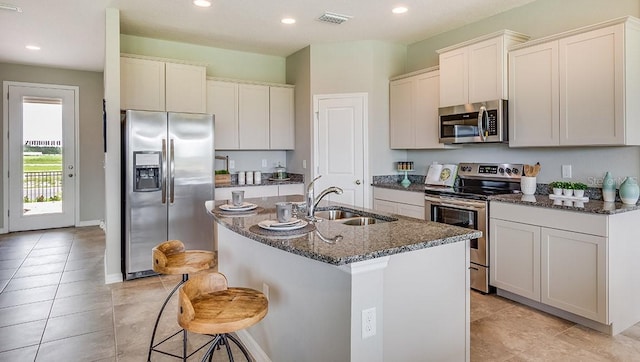 kitchen featuring sink, a kitchen island with sink, white cabinetry, dark stone countertops, and stainless steel appliances