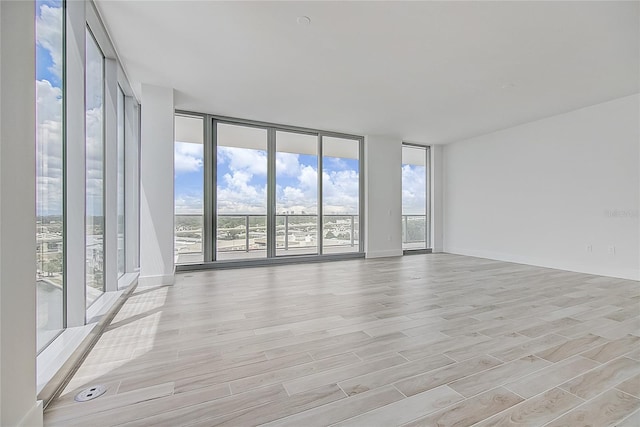 unfurnished room featuring light wood-style flooring, expansive windows, and baseboards