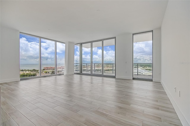 spare room with baseboards, light wood-type flooring, a water view, and floor to ceiling windows