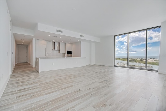 unfurnished living room with a water view, light wood-type flooring, floor to ceiling windows, and visible vents