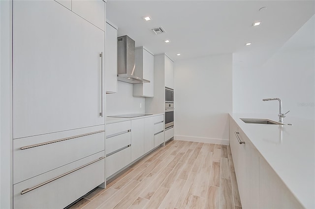 kitchen featuring stainless steel appliances, white cabinetry, wall chimney range hood, and modern cabinets