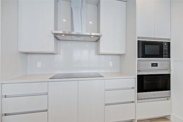 kitchen with stainless steel appliances, wall chimney exhaust hood, light countertops, and white cabinetry