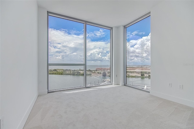 carpeted empty room with floor to ceiling windows, a water view, and baseboards