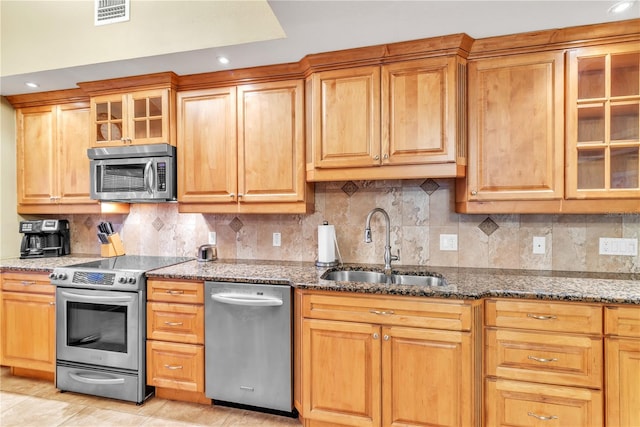 kitchen featuring appliances with stainless steel finishes, dark stone countertops, sink, and tasteful backsplash