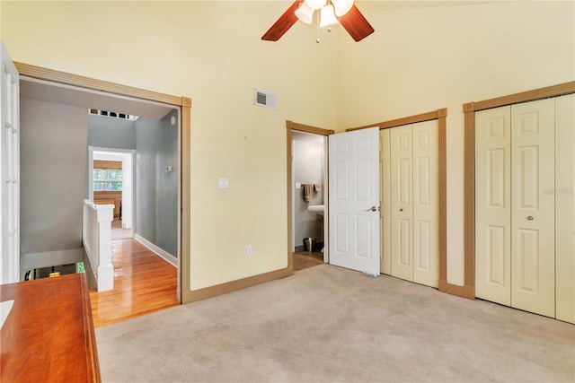 unfurnished bedroom with ceiling fan, multiple closets, light carpet, and a towering ceiling