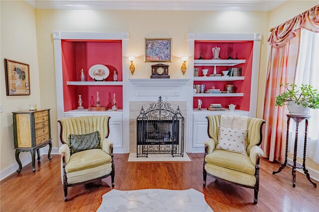 living area with wood-type flooring, ornamental molding, and built in shelves