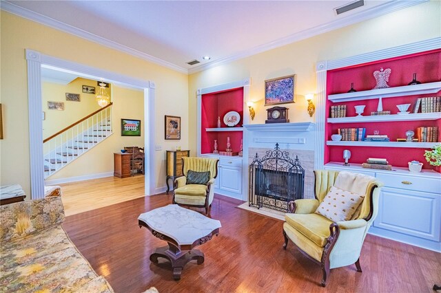 living area with built in shelves, crown molding, and wood-type flooring