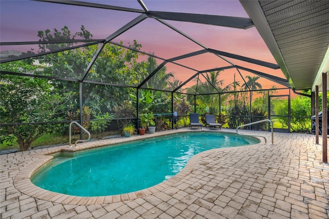 pool at dusk featuring glass enclosure and a patio area