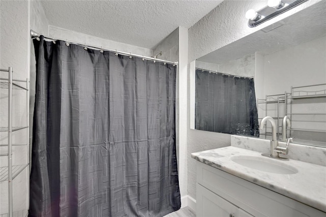 full bath with a shower with curtain, a textured wall, vanity, and a textured ceiling